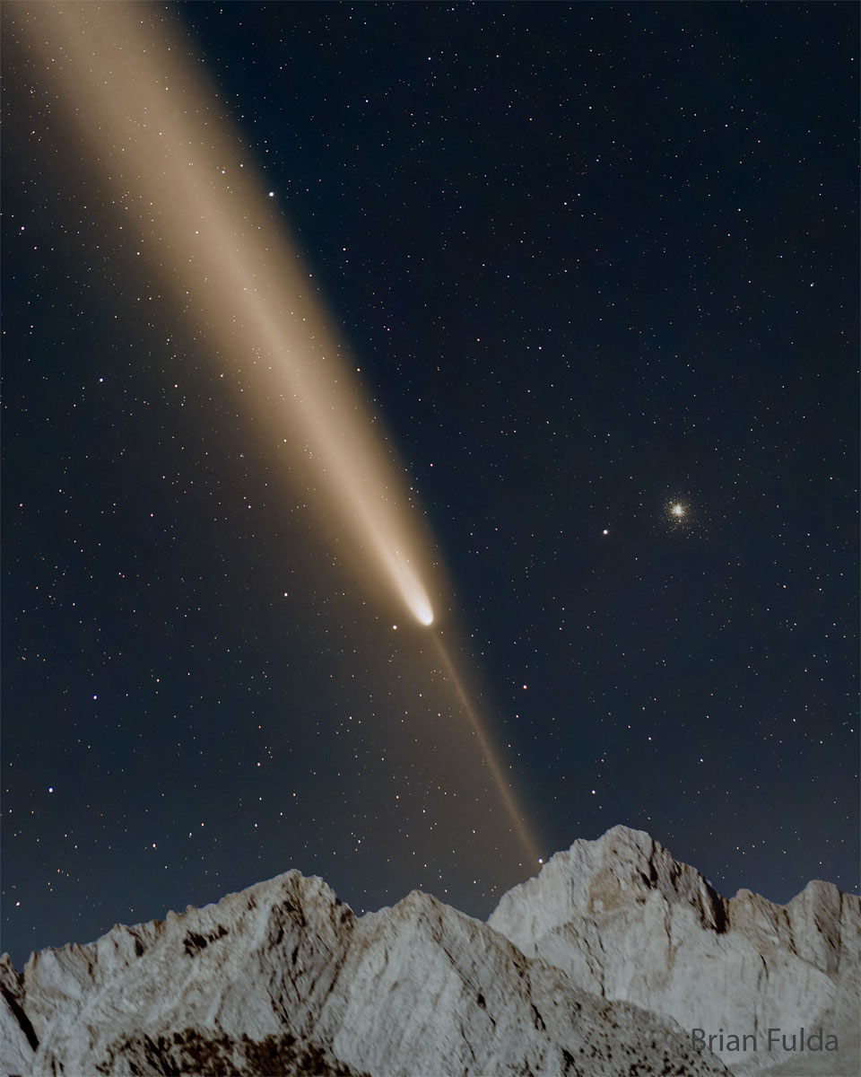 星空下有一颗明亮的彗星。彗星的彗尾指向左上方，而细长的反彗尾指向右下方。前景底部可见山峰。有关更多详细信息，请参阅说明。