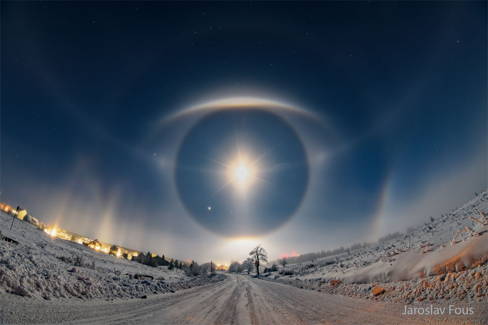 一条被积雪覆盖的道路拾级而上，通向满天繁星。前方天空中的光弧和光晕看起来就像一只巨大的眼睛。有关更多详细信息，请参阅说明。